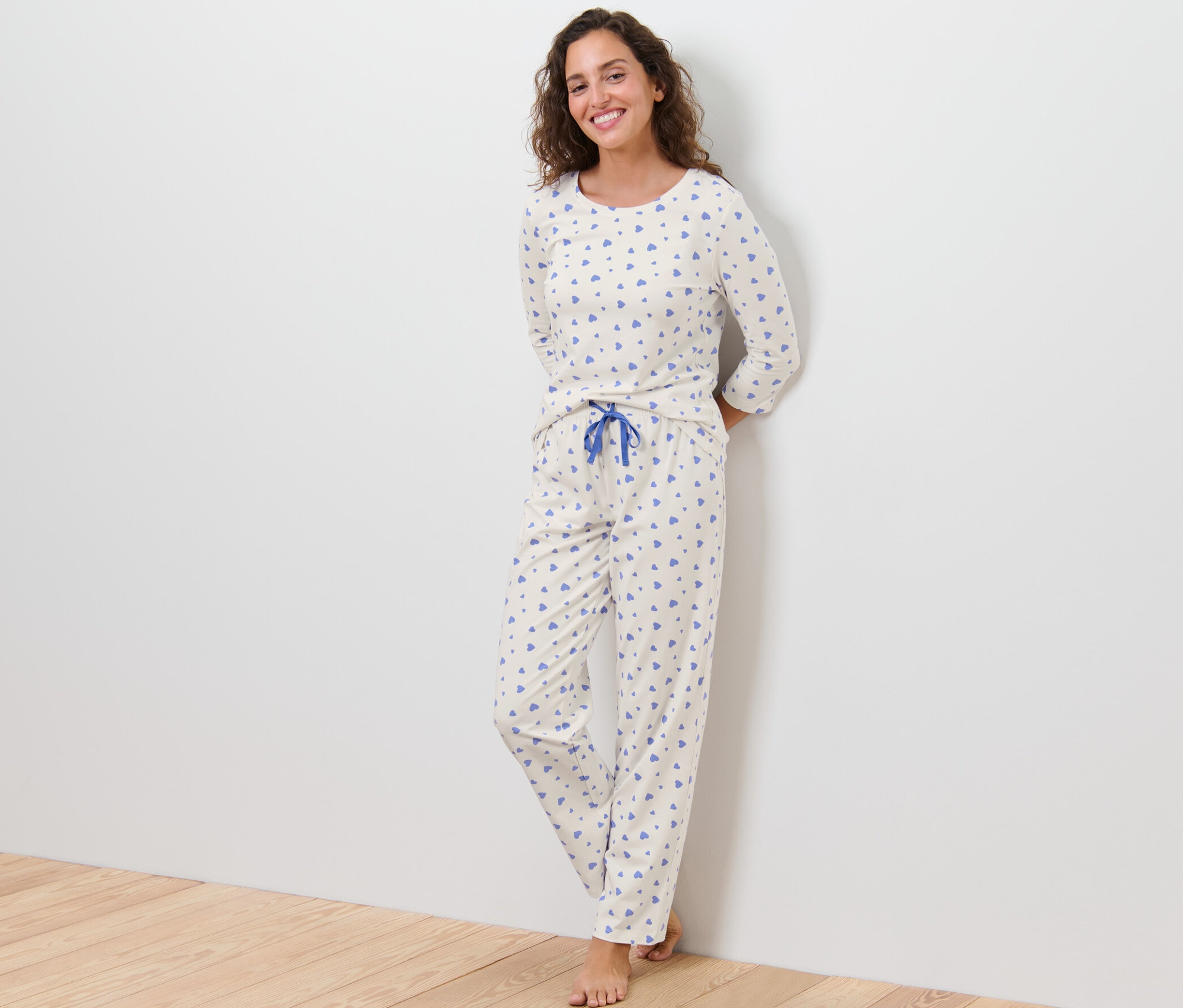 Žena stojí opřená o zeď a má na sobě pyžamo se srdíčky.