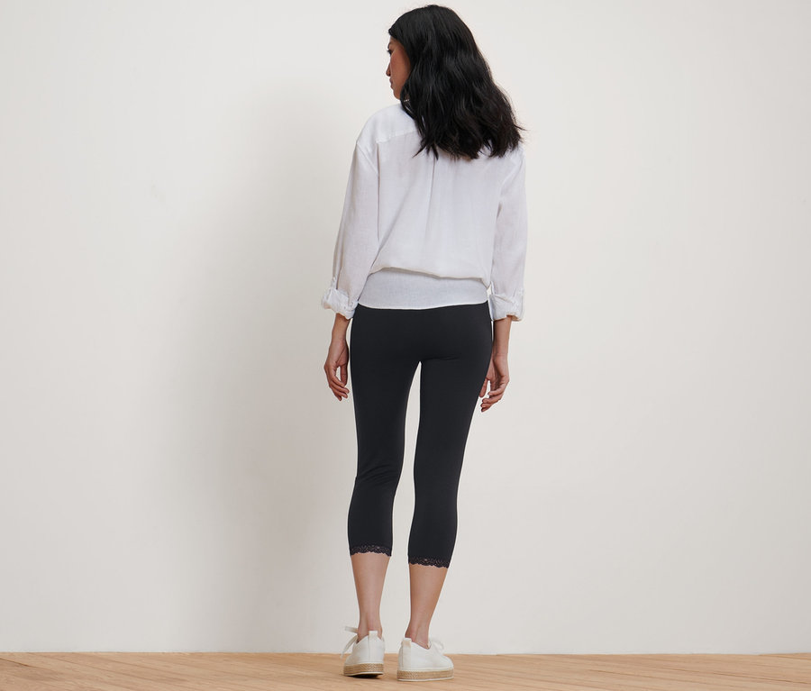 Žena stojí zády k fotoaparátu a má na sobě černé 3/4 legíny s krajkovým lemem.