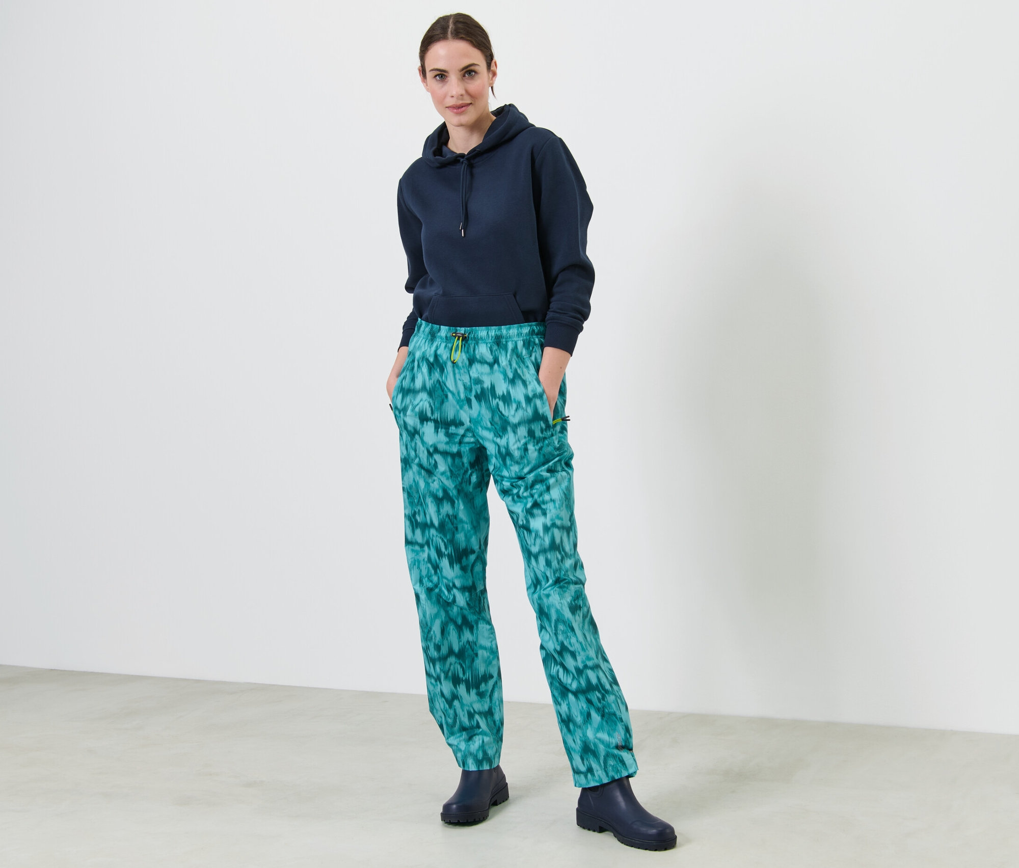 Žena stojí a má ruce v kapsách kalhot do deště s celoplošným potiskem.