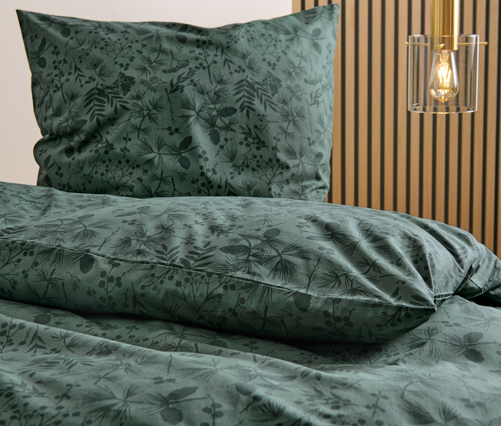 Detail perkálového povlečení se vzorem listů a květin.