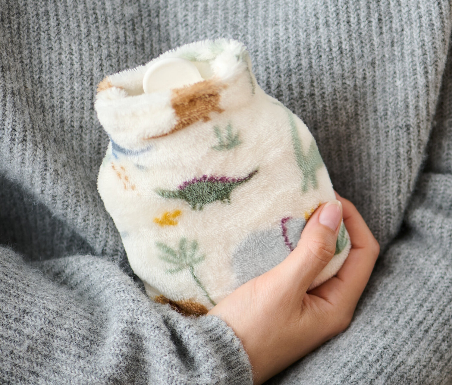 Osoba v šedém svetru drží mini termofor s dinosaury.