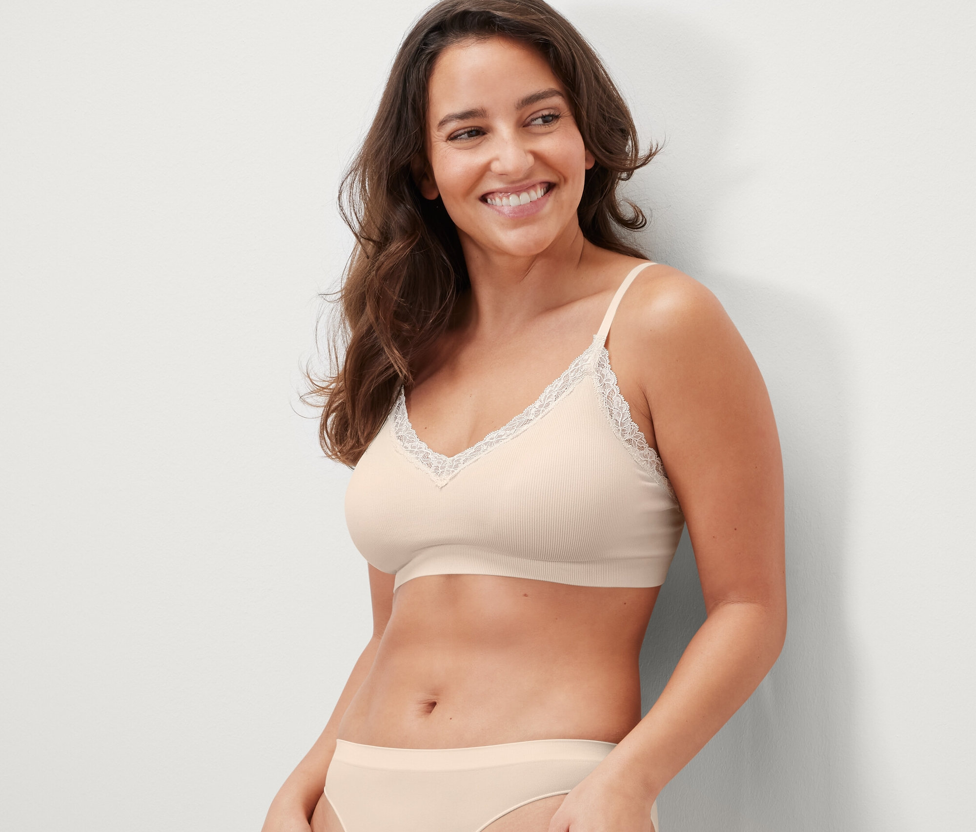 Usmívající se žena má na sobě krémovou bezešvou podprsenku s krajkou.