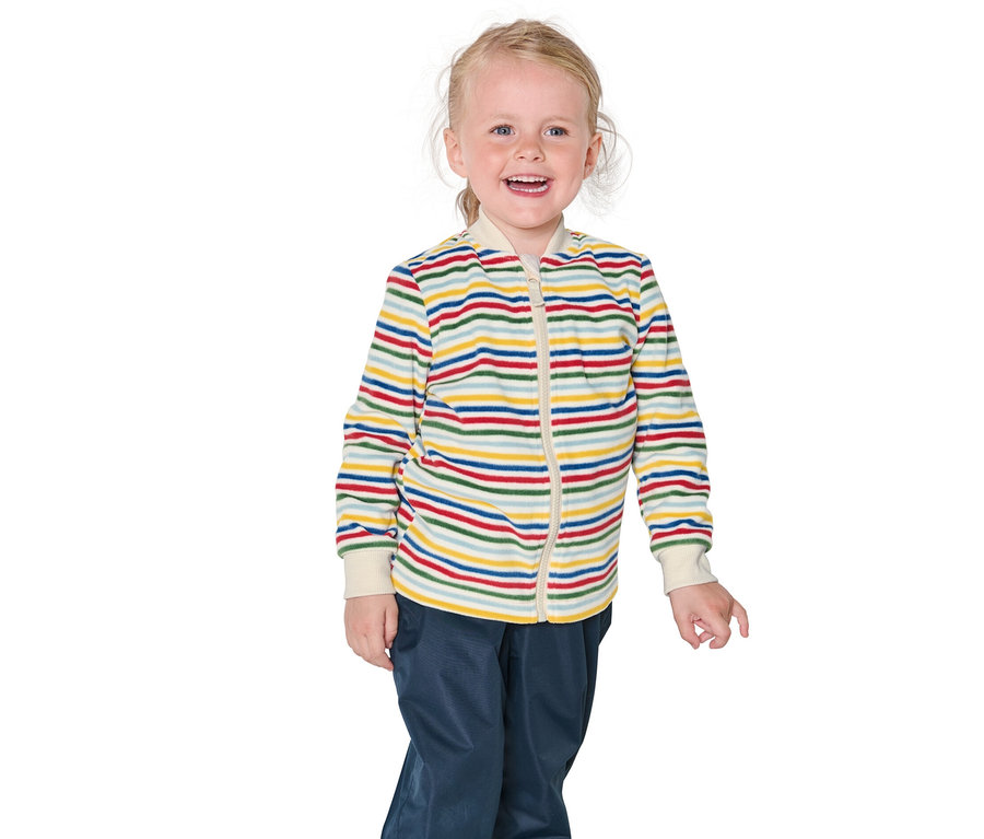 Usmívající se blondýnka má na sobě proužkovanou bundu a modré kalhoty.