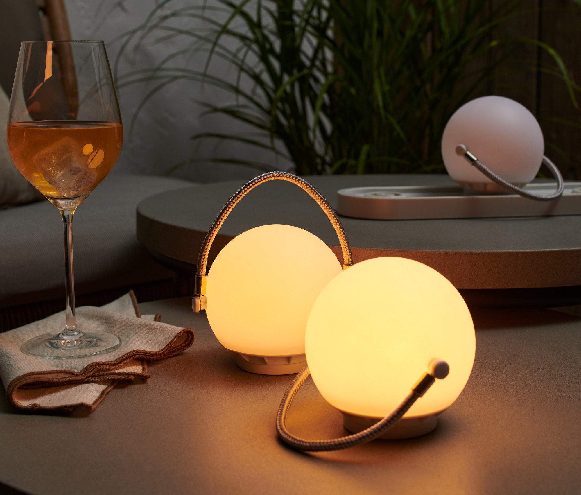 Na stolku stojí sada stolních lamp na akumulátor, vedle sklenice s pitím.