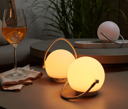 Na stolku stojí sada stolních lamp na akumulátor, vedle sklenice s pitím.