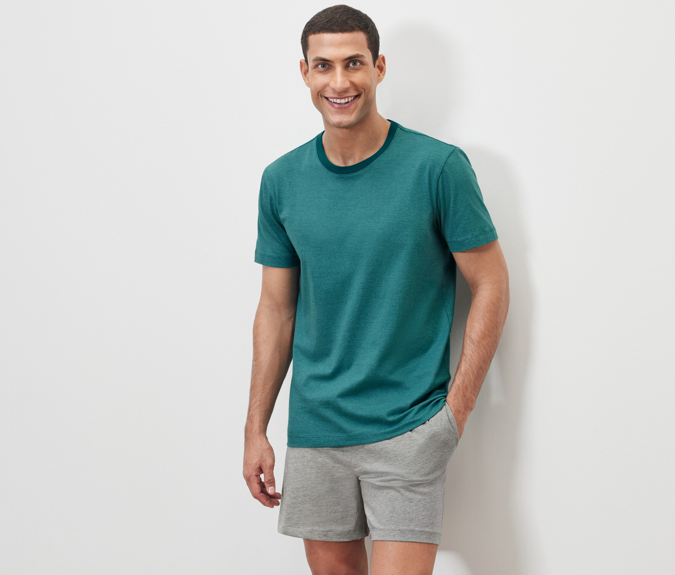 Muž pózuje na bílém pozadí v krátkém pyžamu.