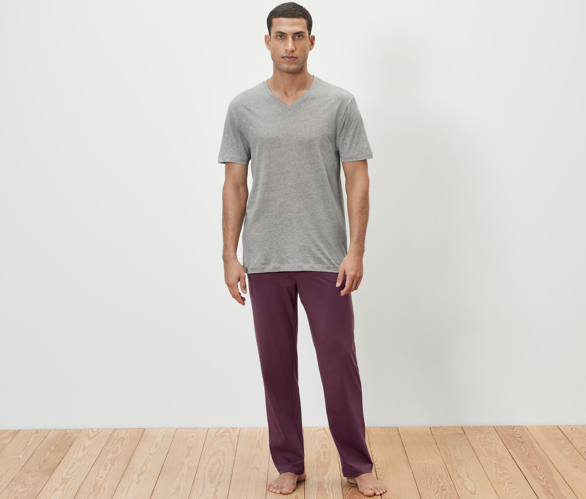 Muž má na sobě šedé tričko a vínově červené pyžamové kalhoty.