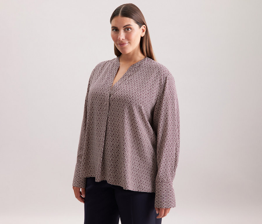 Žena má na sobě tuniku z viskózy Seidensticker s celoplošným potiskem v barvě ecru a burgundské.