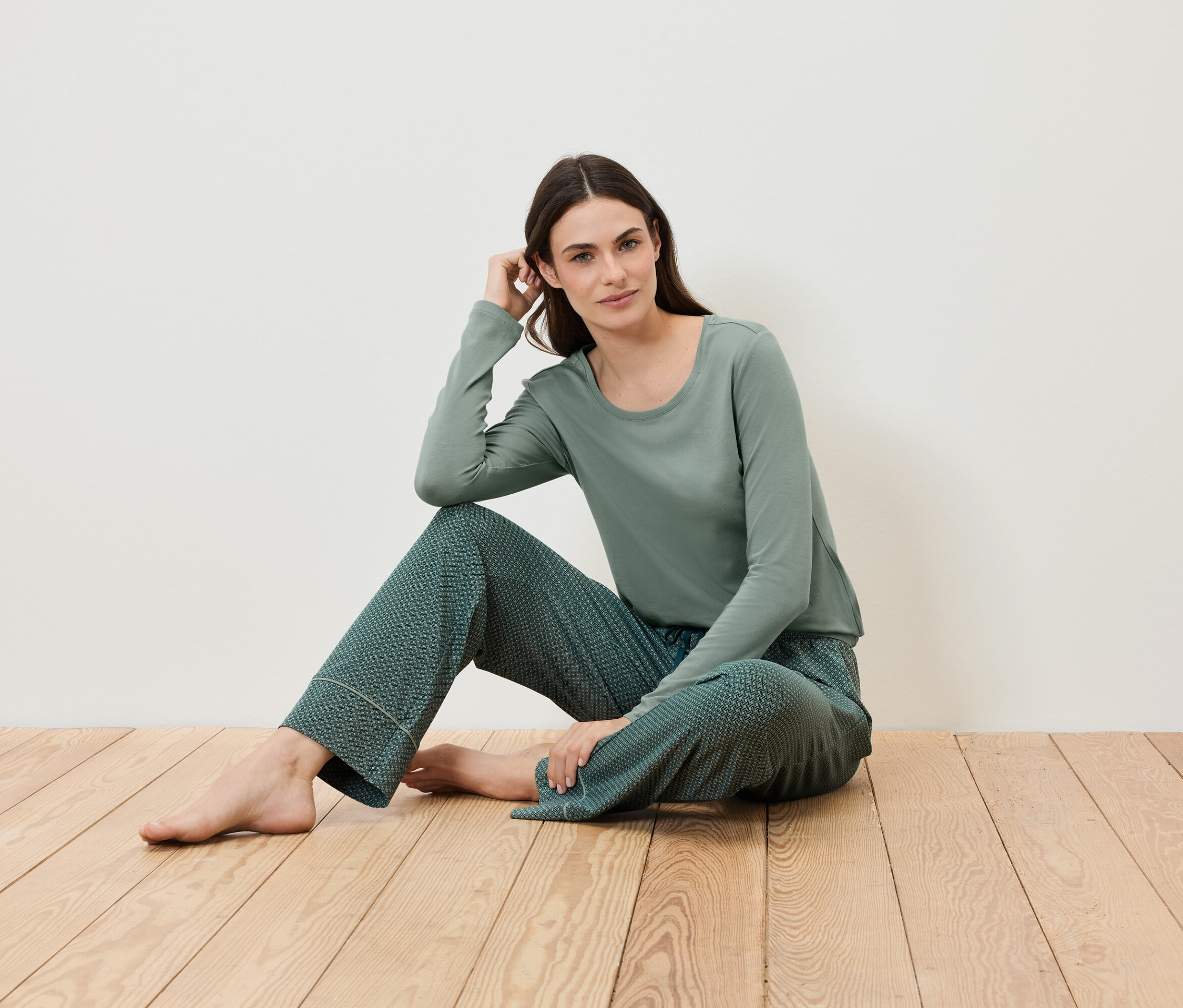 Žena sedí na dřevěné podlaze a má na sobě zelené pyžamo.