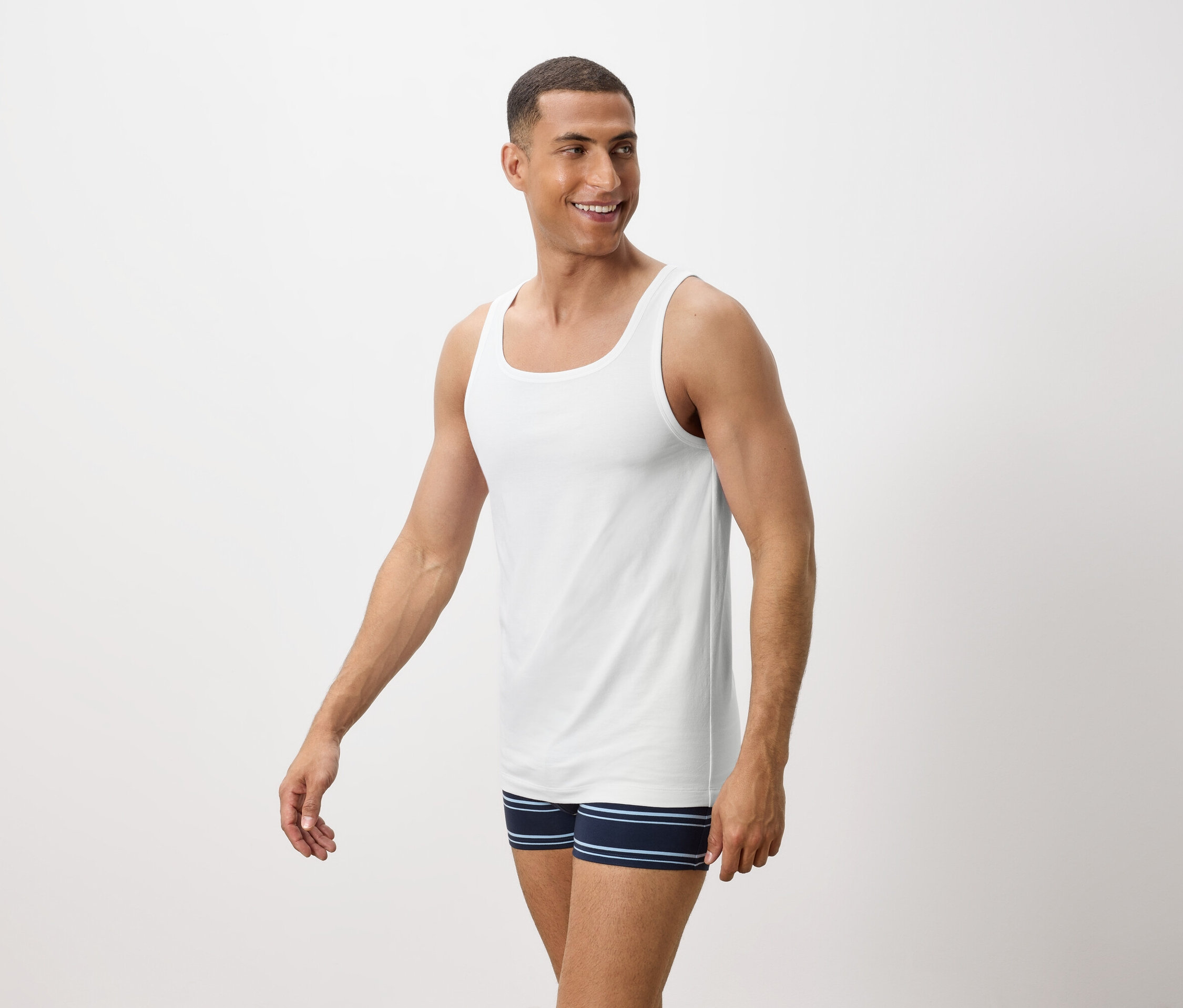 Muž usmívá se a má na sobě bílé tílko a modré pruhované boxerky.