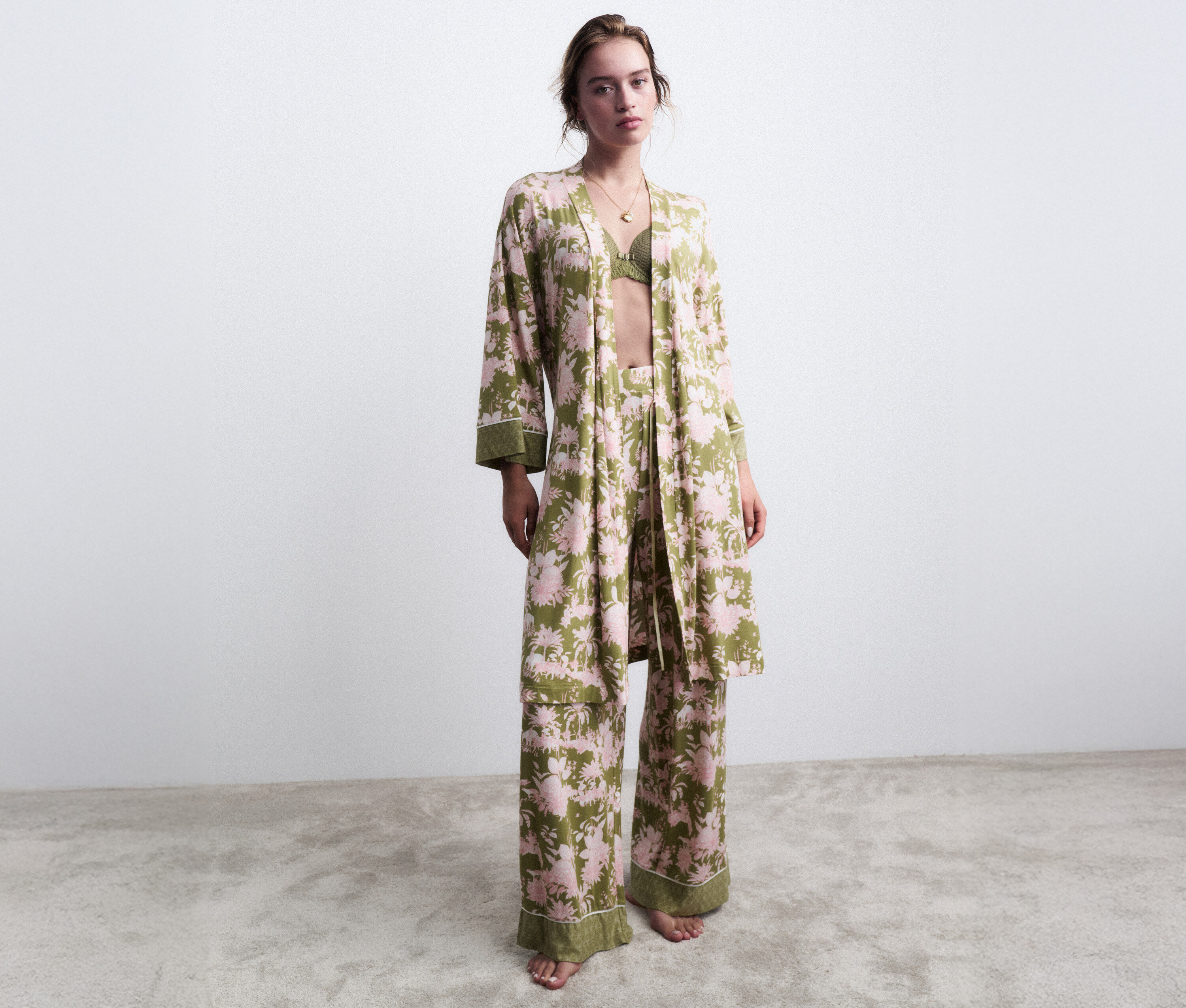 Žena stojí bosá v zeleném květinovém pyžamu s odpovídajícím županem.