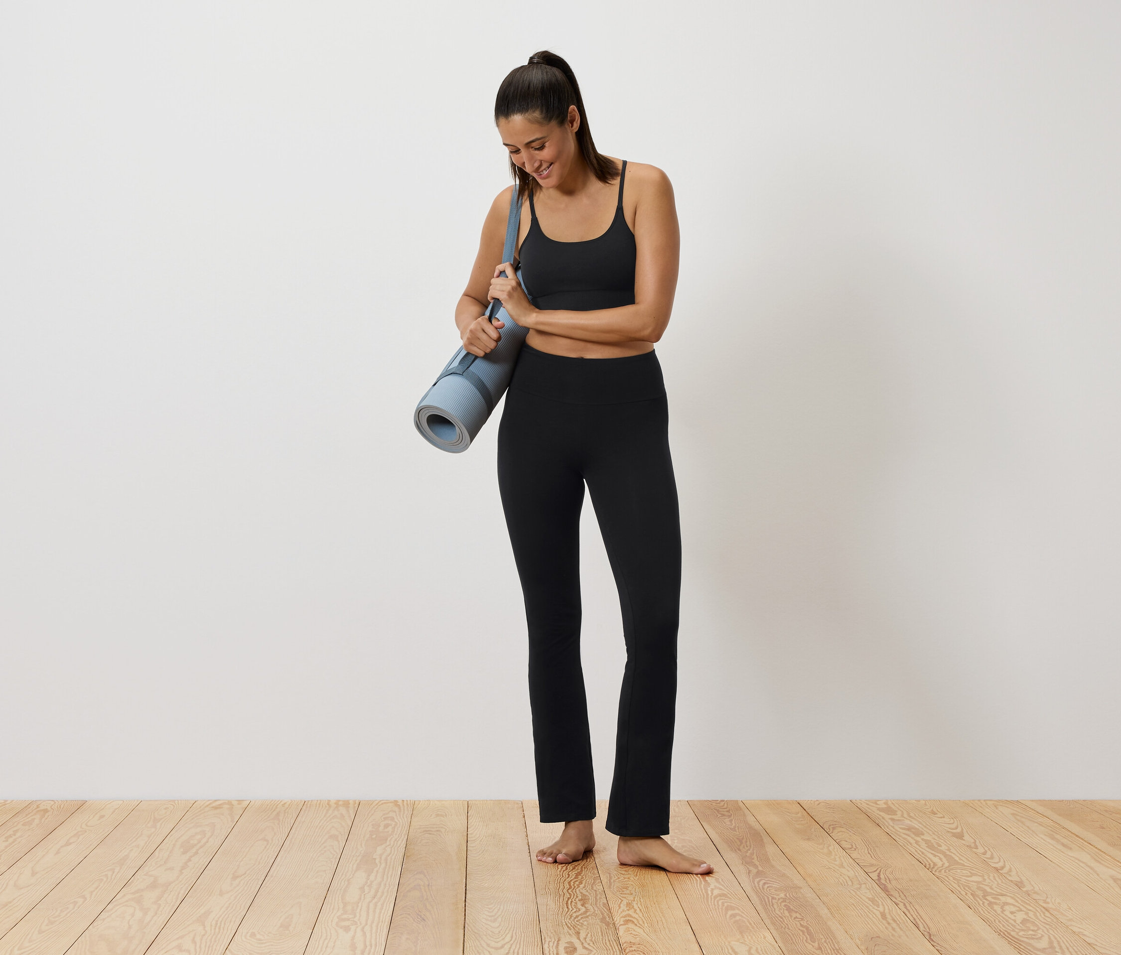 Žena v černém sportovním oblečení drží podložku na cvičení.