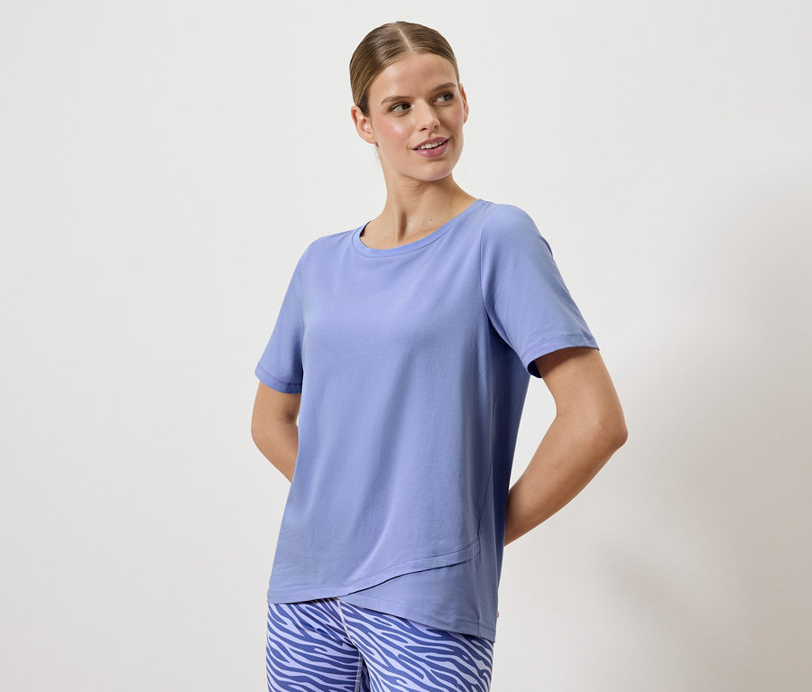 Žena pózuje v modrém tričku a kalhotách se zvířecím vzorem.