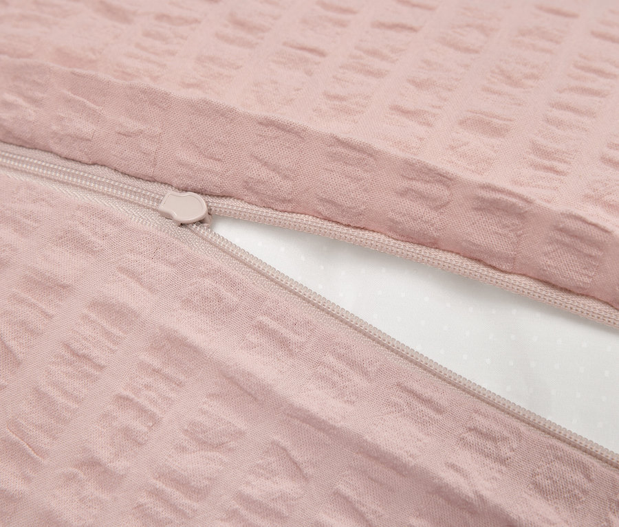 Detail růžového povlečení s texturou a zipem, částečně odhaleným bílým vnitřkem.
