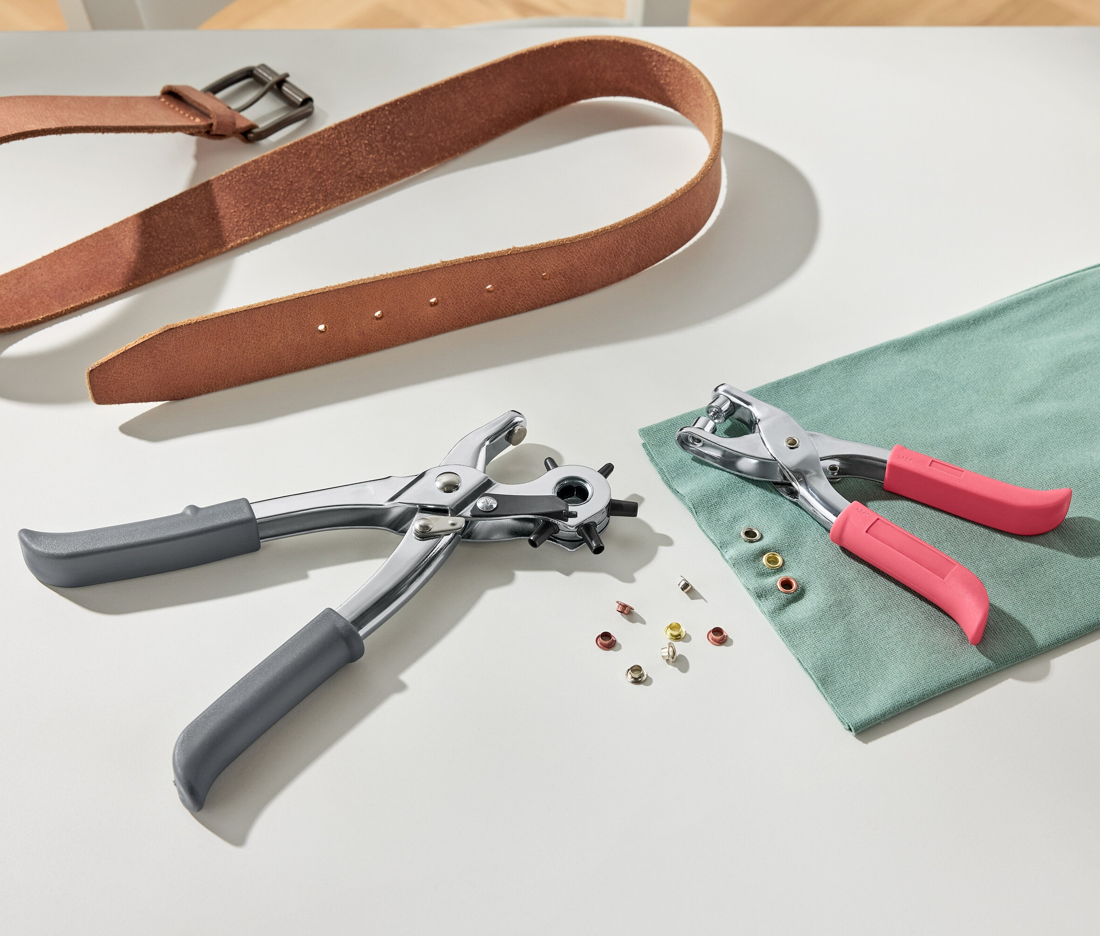 Hnědý kožený pásek a děrovací kleště na bílém pozadí.