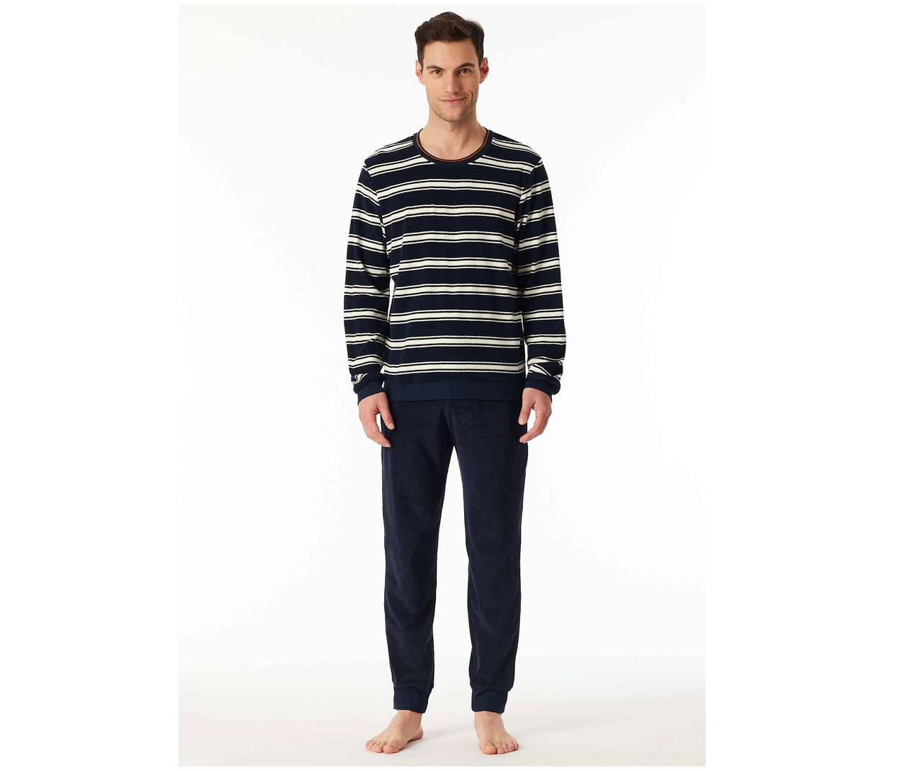 Muž stojí a má na sobě pruhované tričko s dlouhým rukávem a tmavě modré sametové kalhoty.