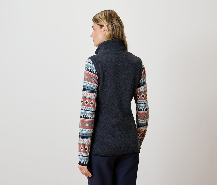 Žena zády k fotoaparátu má na sobě tmavě šedou fleecovou vestu a modré kalhoty.