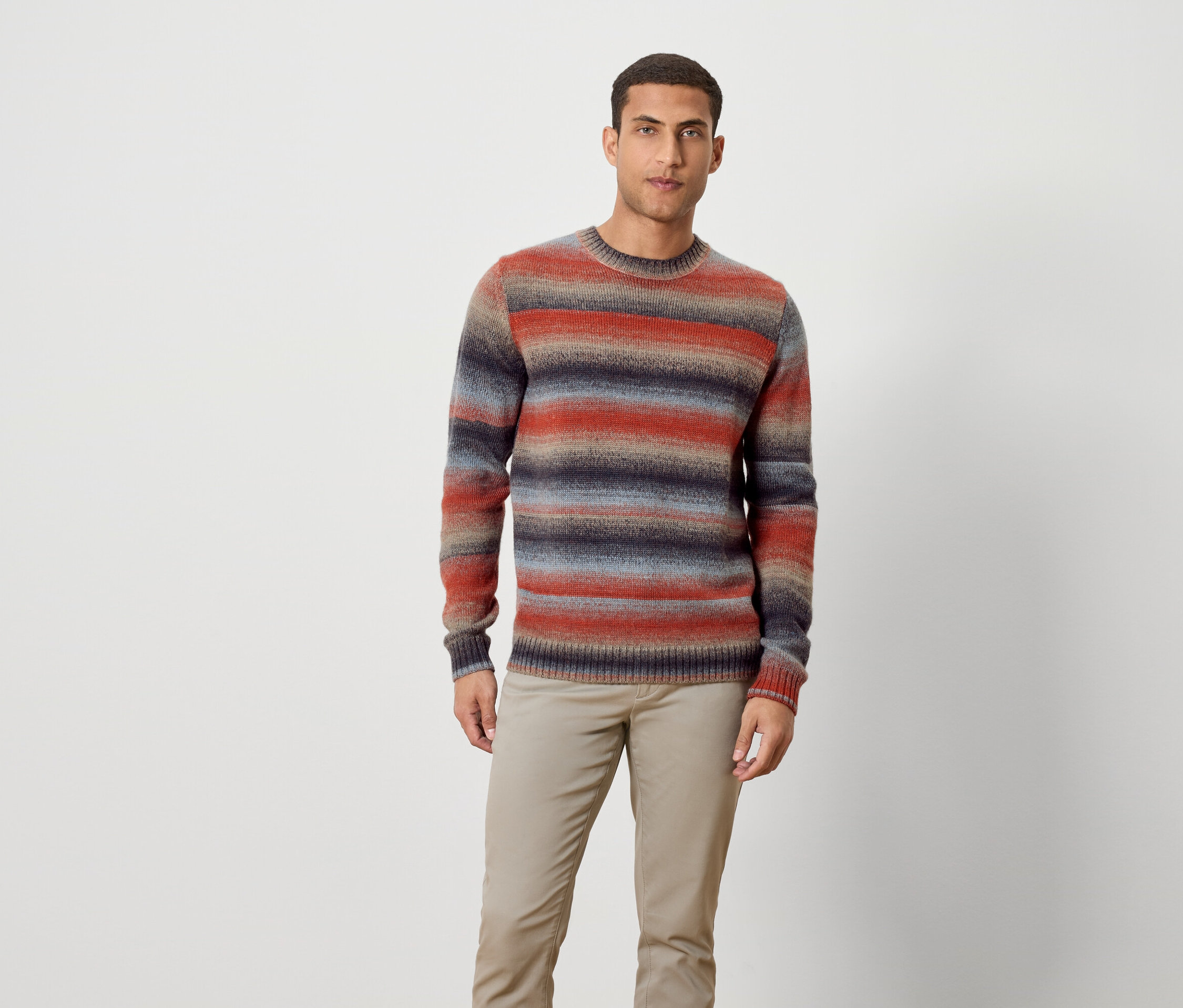Muž stojí a má na sobě pruhovaný svetr a kalhoty.