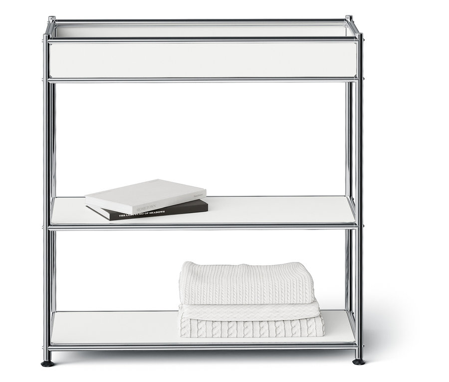 Chromovaný regál se třemi bílými policemi. Na prostřední polici leží dvě knihy a na spodní polici jsou složené bílé ručníky.