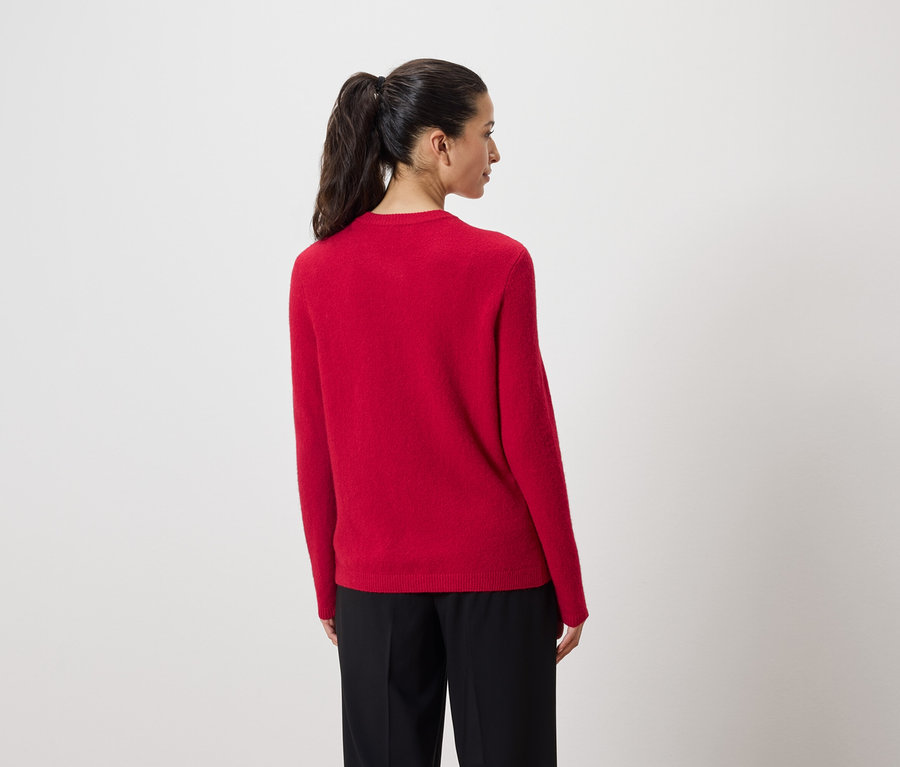 Žena zády k fotoaparátu má na sobě červený svetr a černé kalhoty.