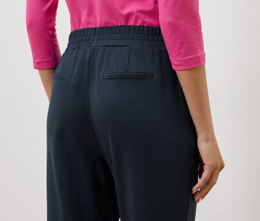 Detailní záběr na záda ženy v tmavě modrých kalhotách a růžové halence.