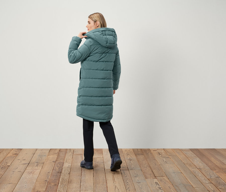 Žena v dlouhé prošívané bundě s kapucí, zády ke kameře.