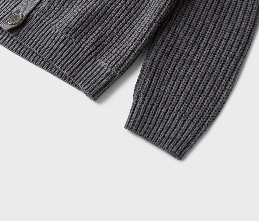 Detailní pohled na šedý pletený kardigan s knoflíkem.