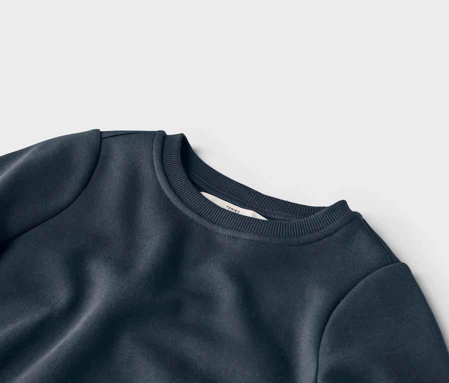 Detailní pohled na tmavě modrou mikinu s kulatým výstřihem a štítkem značky Tchibo u límce.