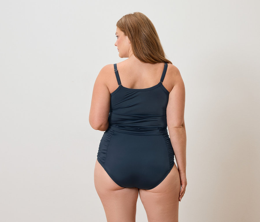 Pohled zezadu na ženu s dlouhými hnědými vlasy v tmavě modrých plavkách.