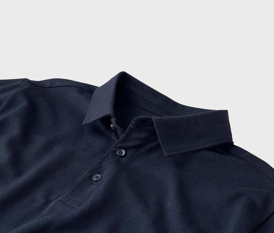 Detailní záběr na tmavě modré polo tričko s límcem a třemi knoflíky na světle šedém pozadí.