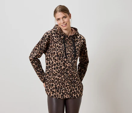 Žena má na sobě hnědou leopardí mikinu s kapucí a hnědé kožené legíny.