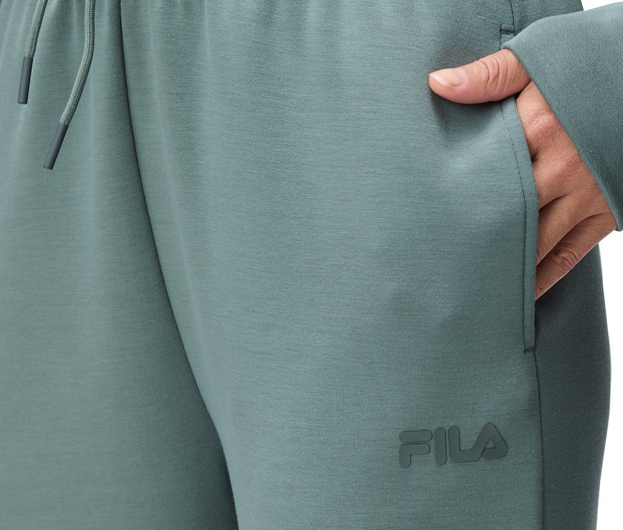 Detailní záběr na osobu v zelených teplácích Fila s elastickým pasem a stahovací šňůrkou a rukou v kapse.