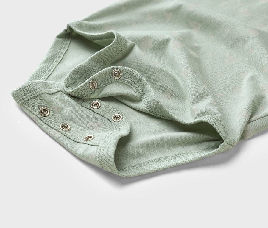 Detailní záběr světle zeleného dětského body s patentkami.