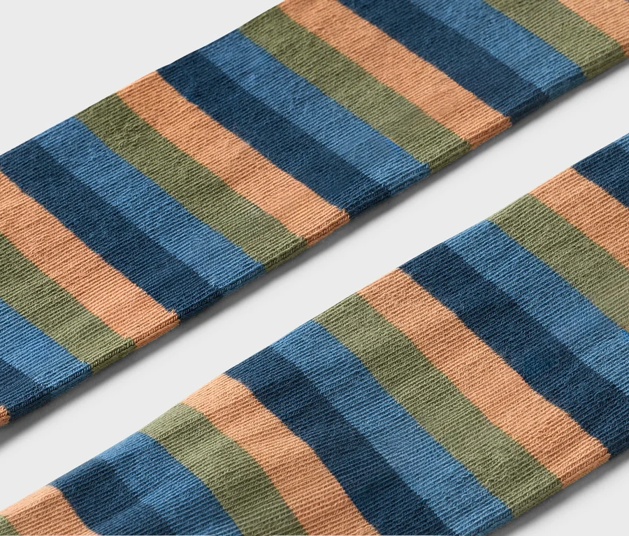 Detail dvou pruhovaných ponožek v oranžové, modré a zelené barvě na šedém pozadí.
