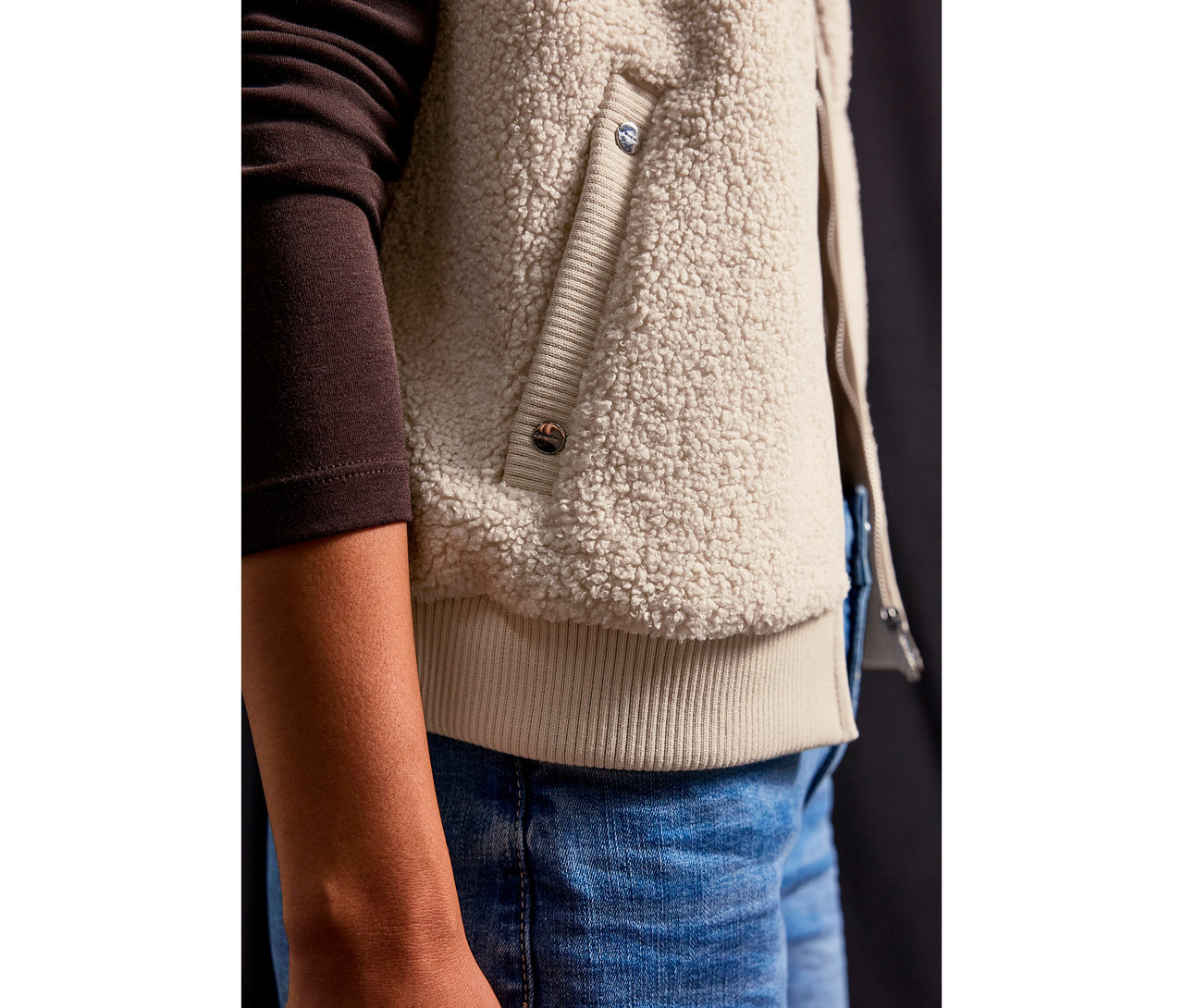 Detail osoby v plyšové vestě Street One a džínách.