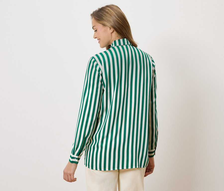 Žena zezadu v zeleno-bílé pruhované halence a béžových kalhotách.