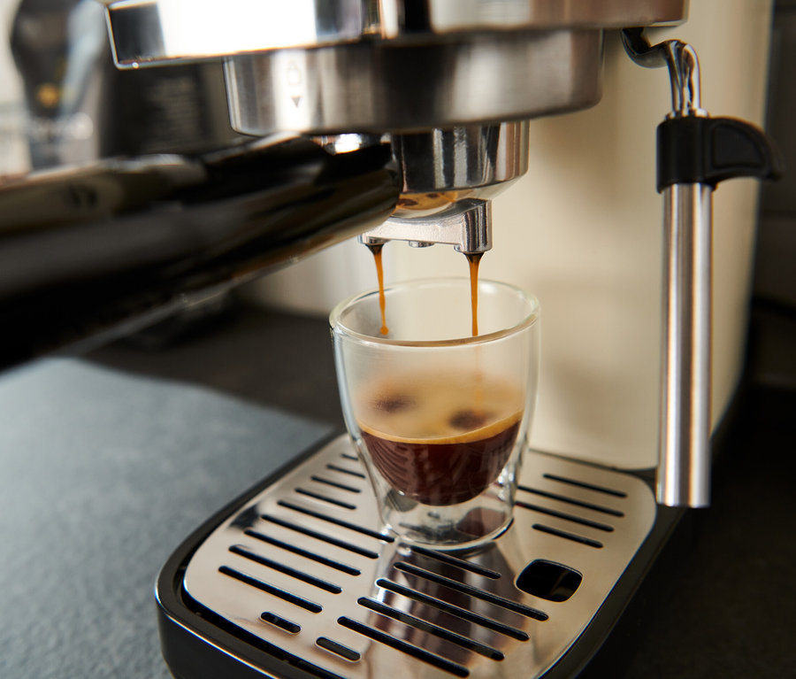 Espresso teče z krémově bílého pákového kávovaru »Lapressa« do sklenice.