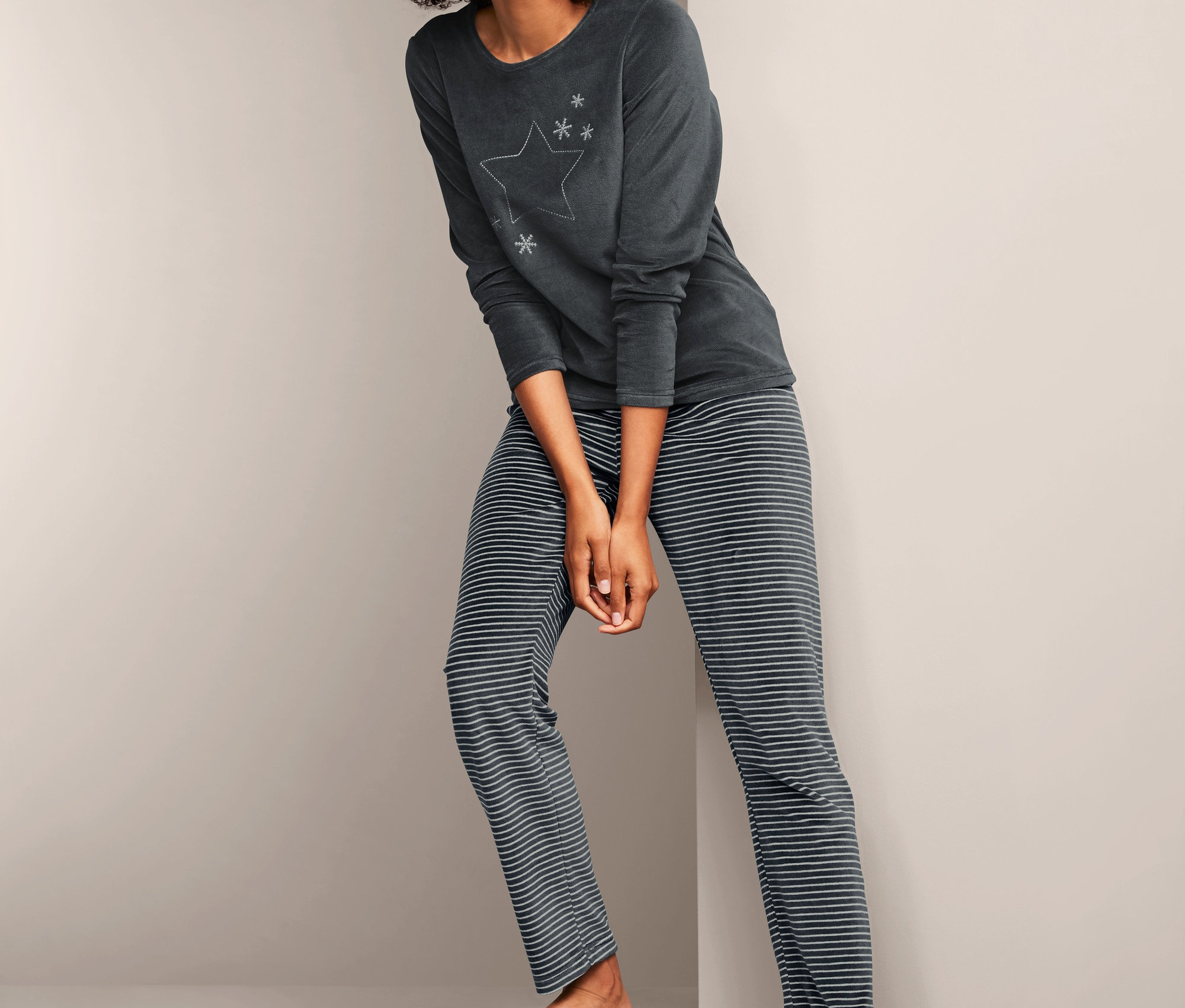 Žena pózuje v plyšovém pyžamu s dlouhým rukávem a pruhovaných kalhotách.