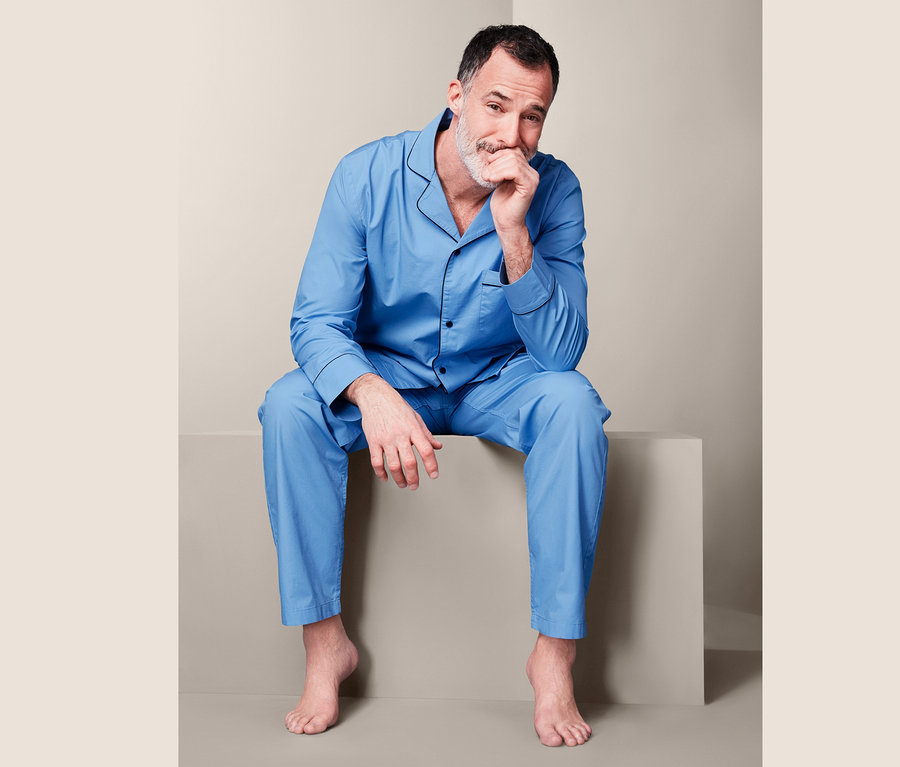 Muž sedí a má ruku na bradě. Oblečený je do modrého tkaného pyžama.