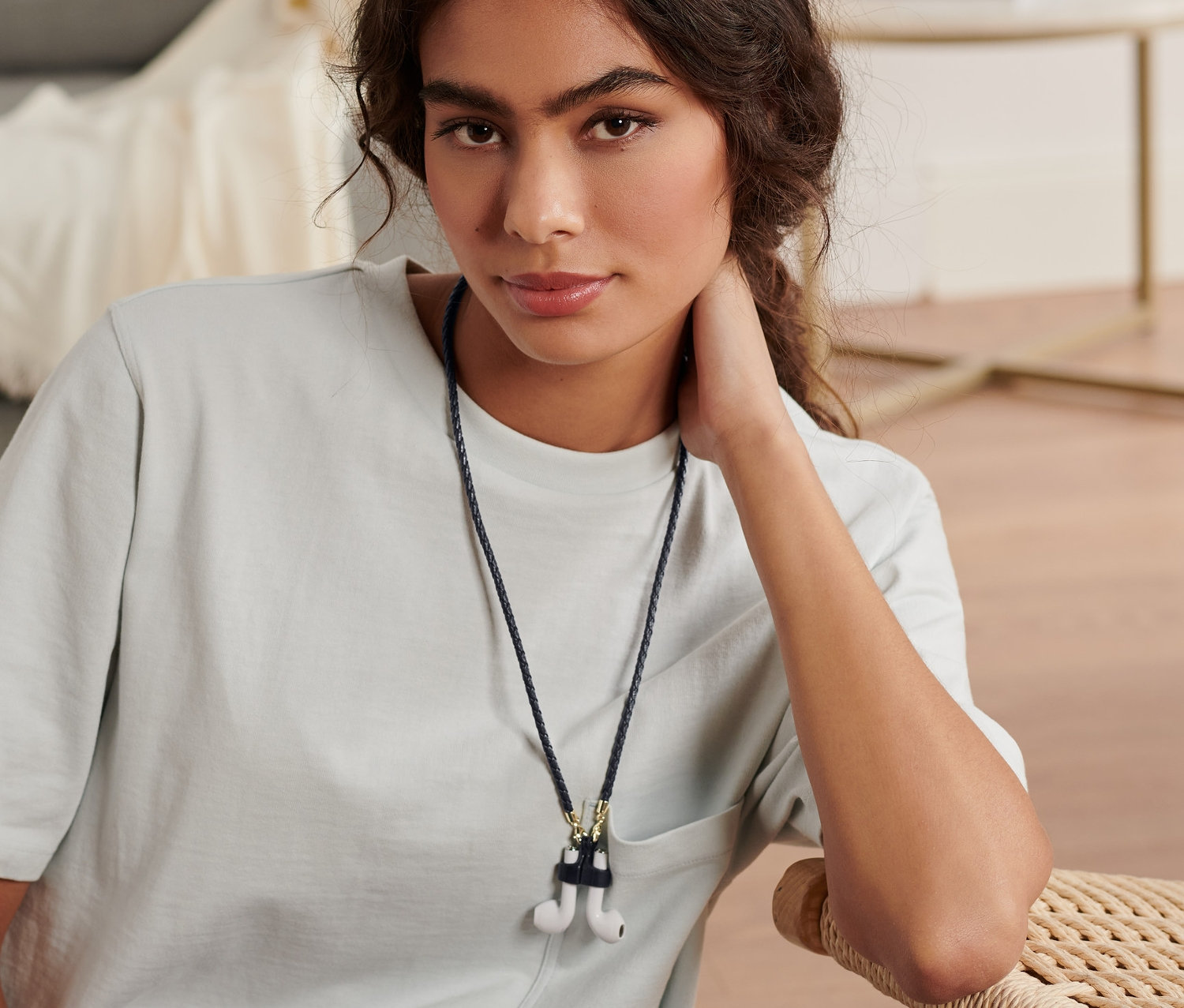 Žena sedí a má na sobě multifunkční šňůrku na brýle, roušky a sluchátka do uší.