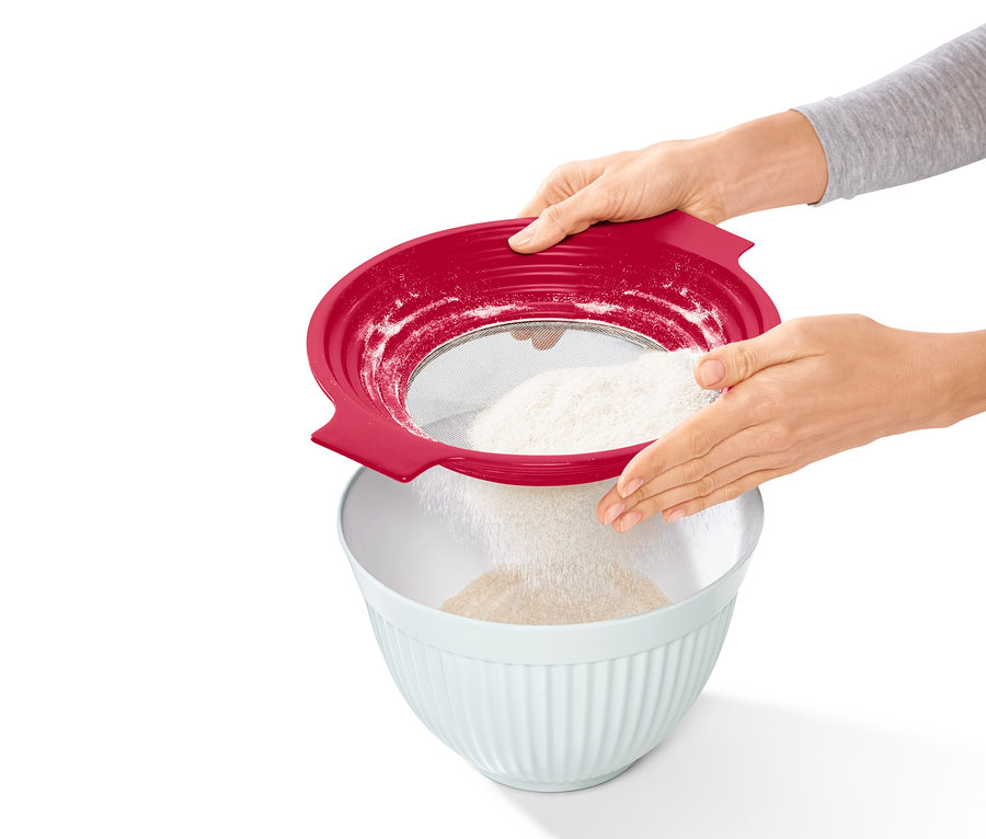 Žena prosévá mouku přes červené sítko 2 v 1 do mísy.