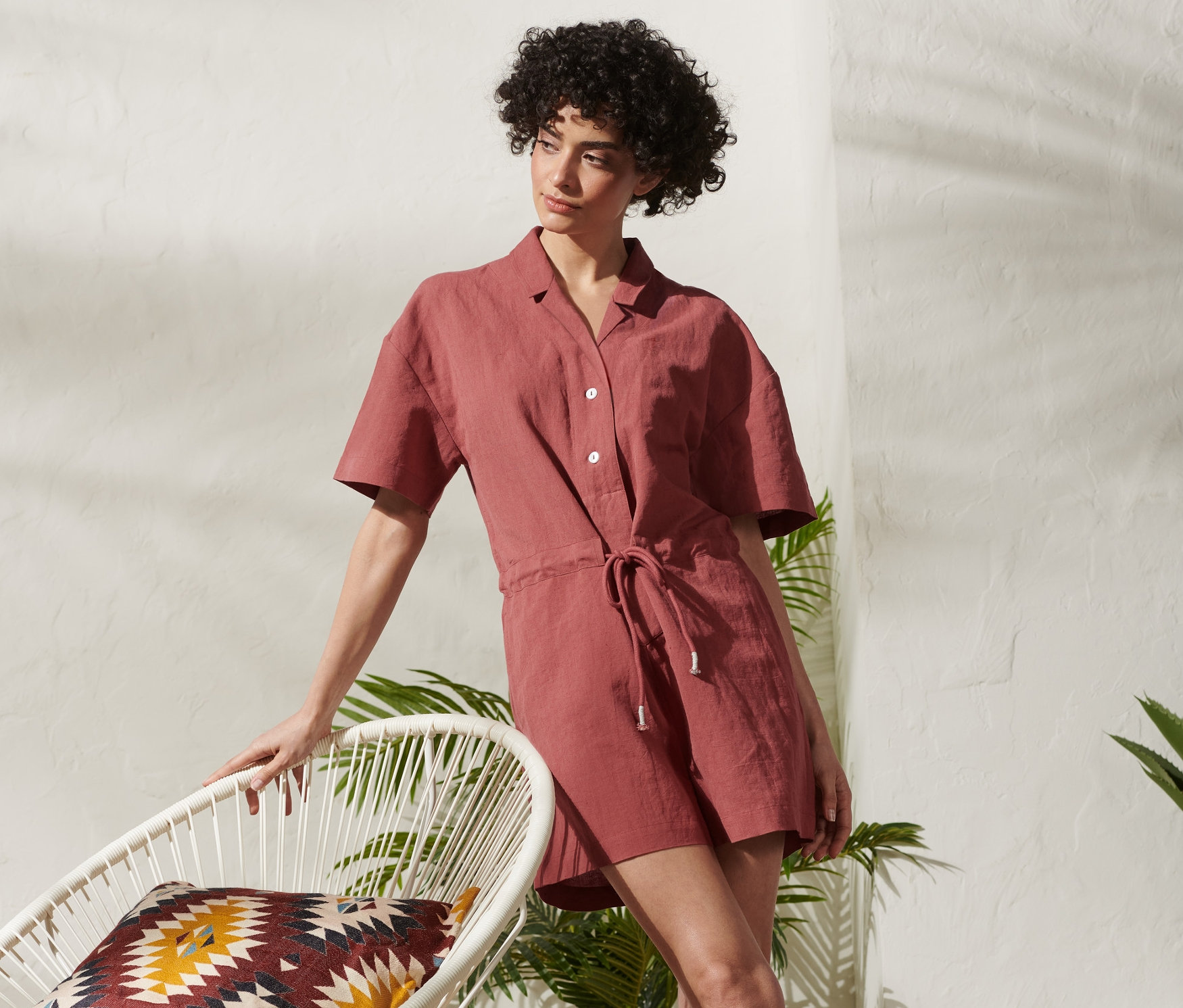 Žena opírající se o bílé křeslo v krátkém overalu.