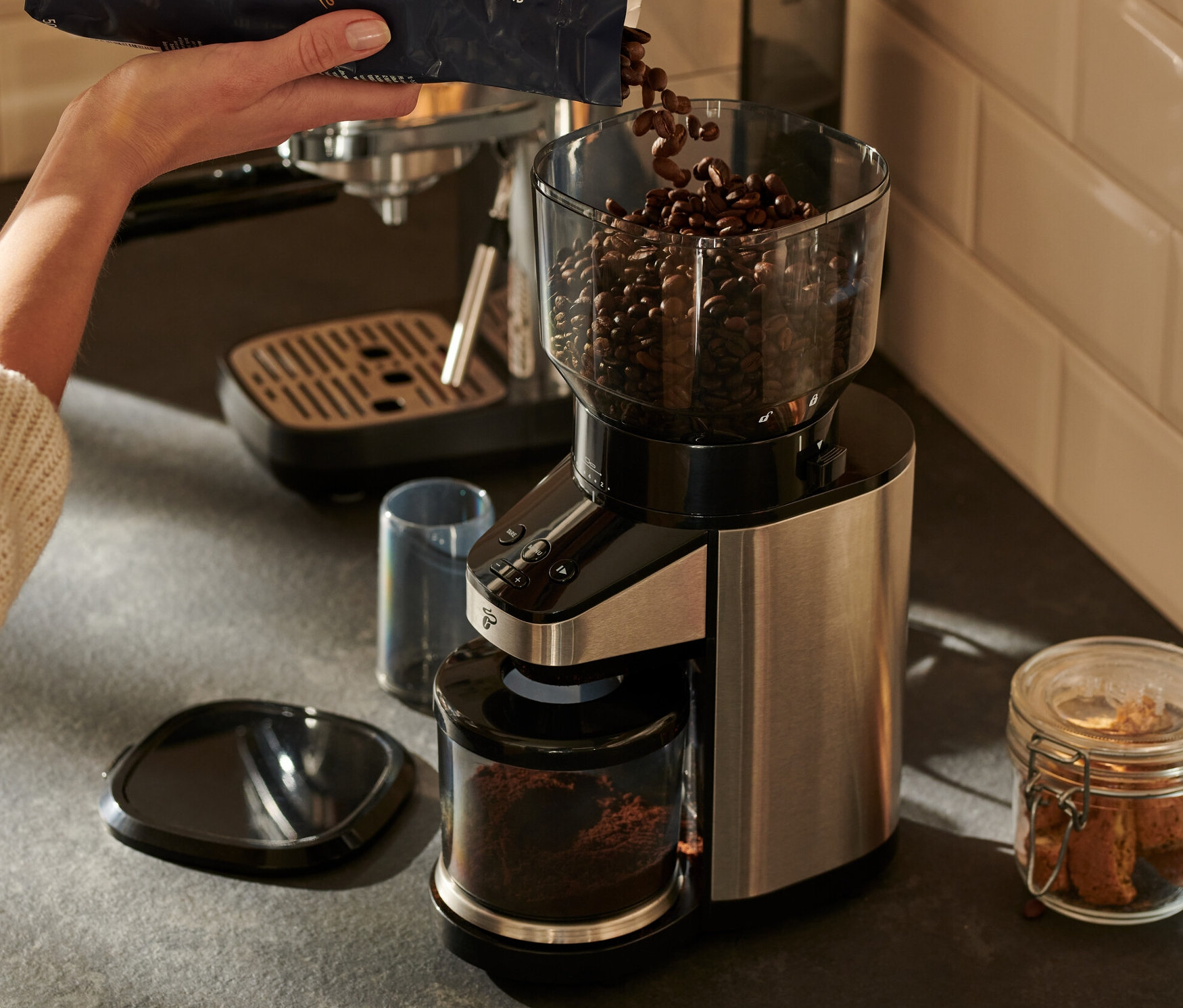 Žena sype kávová zrna do elektrického mlýnku na kávu s váhou.
