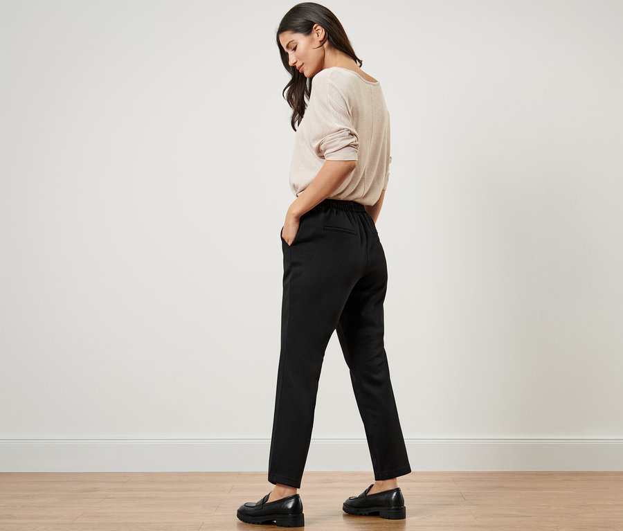 Žena v béžovém svetru a černých joggpant kalhotách.