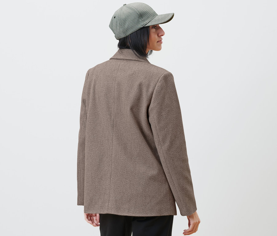 Žena v blejzru a kostkované čepici se dívá doprava.