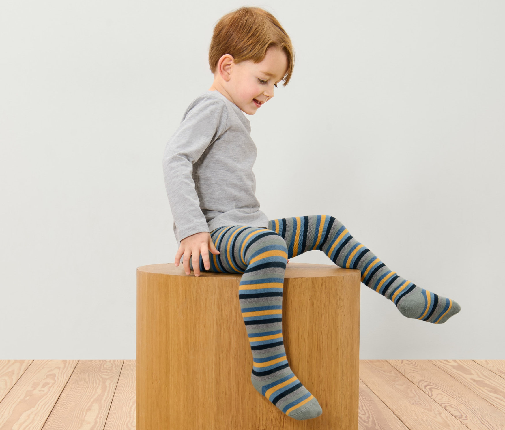 Chlapec sedí na dřevěné stoličce a má na sobě modré pruhované termo punčocháče.