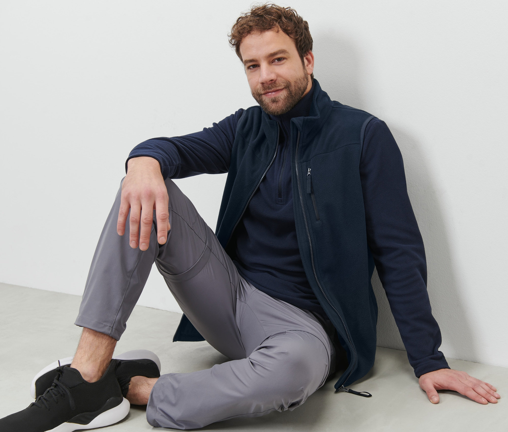 Muž sedí na zemi a má na sobě fleecovou vestu.