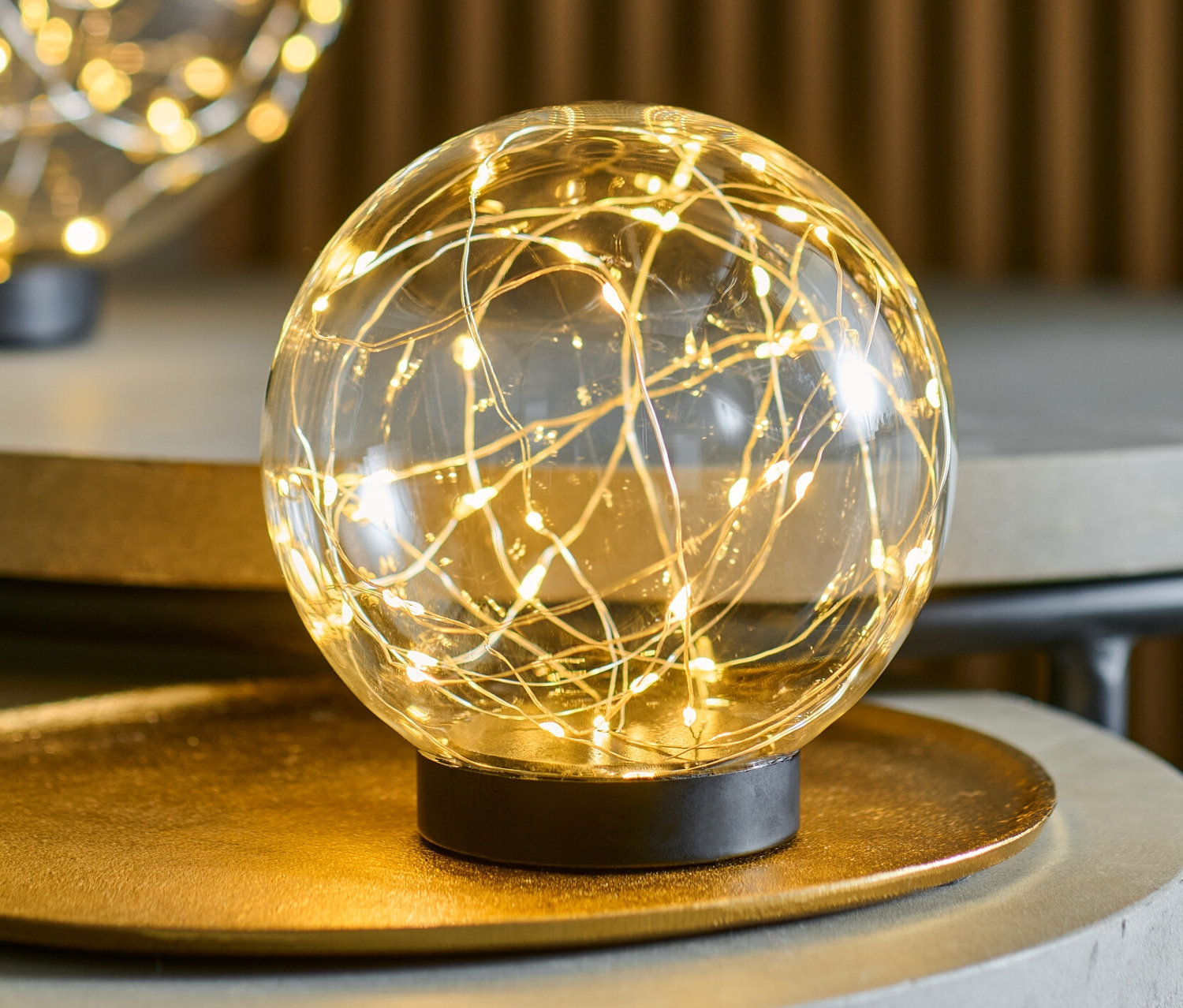 Dvě skleněné koule s LED světýlky, každá o průměru cca 15 cm, stojí na šedých stolcích.