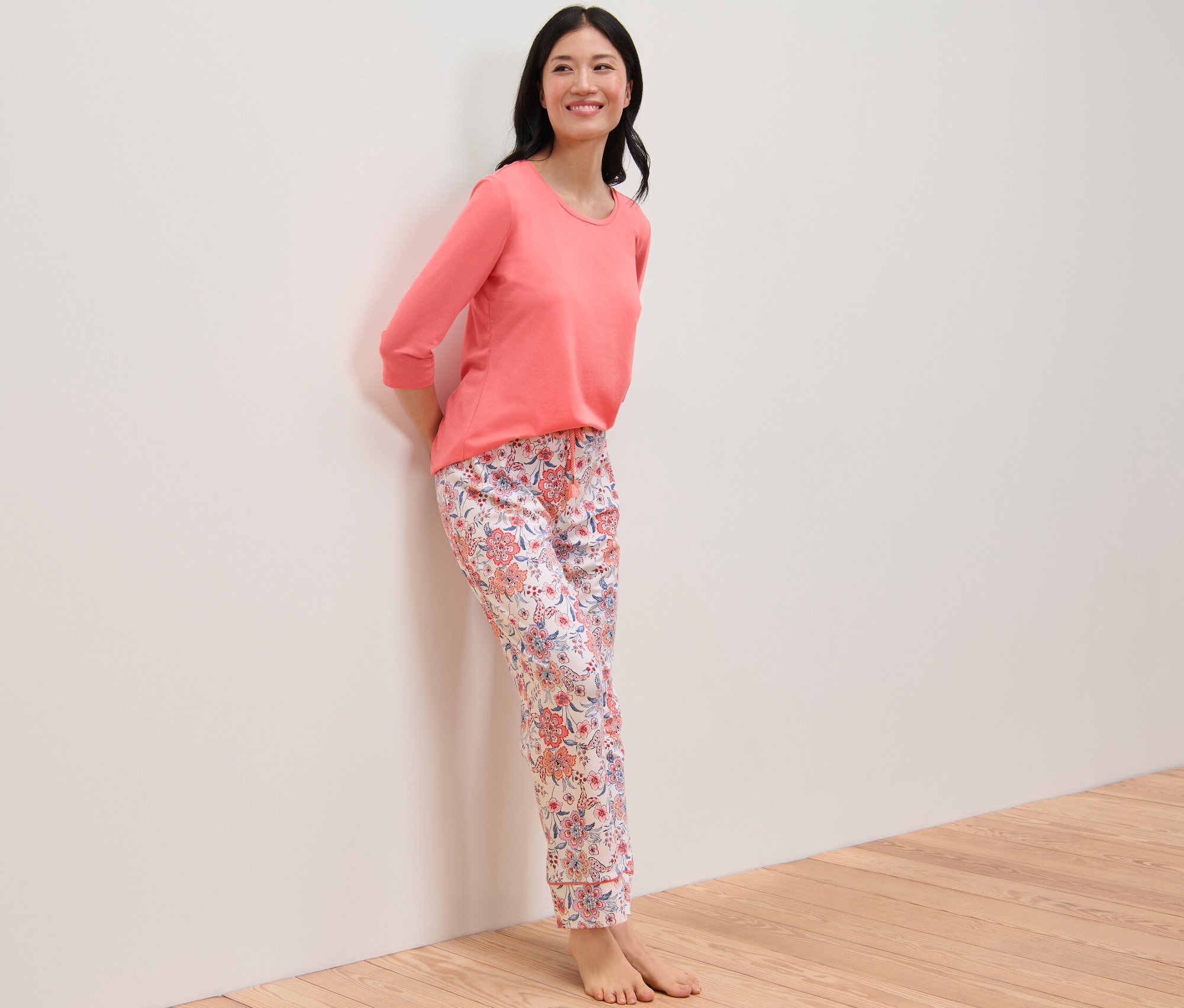Žena v pyžamu s květinovým vzorem stojí opřená o zeď.