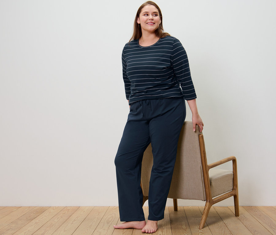 Žena v tmavě modrém pruhovaném pyžamu stojí vedle křesla.